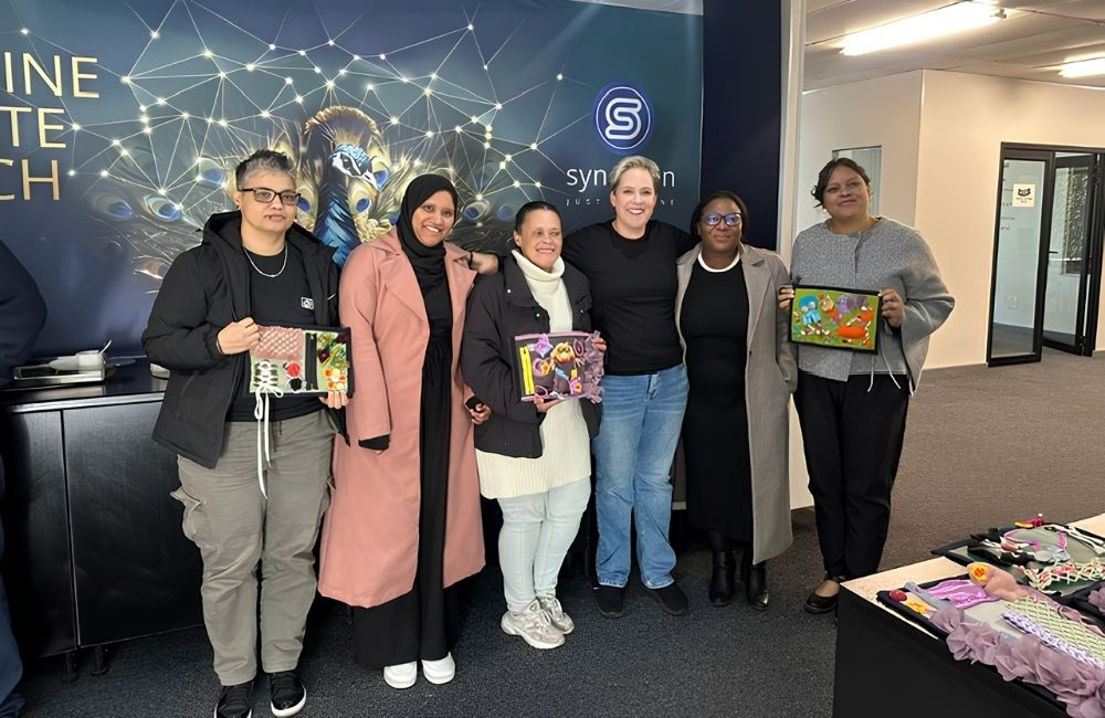 Synchron staff members display twiddle sensory blankets handmade for the company’s Mandela Day project